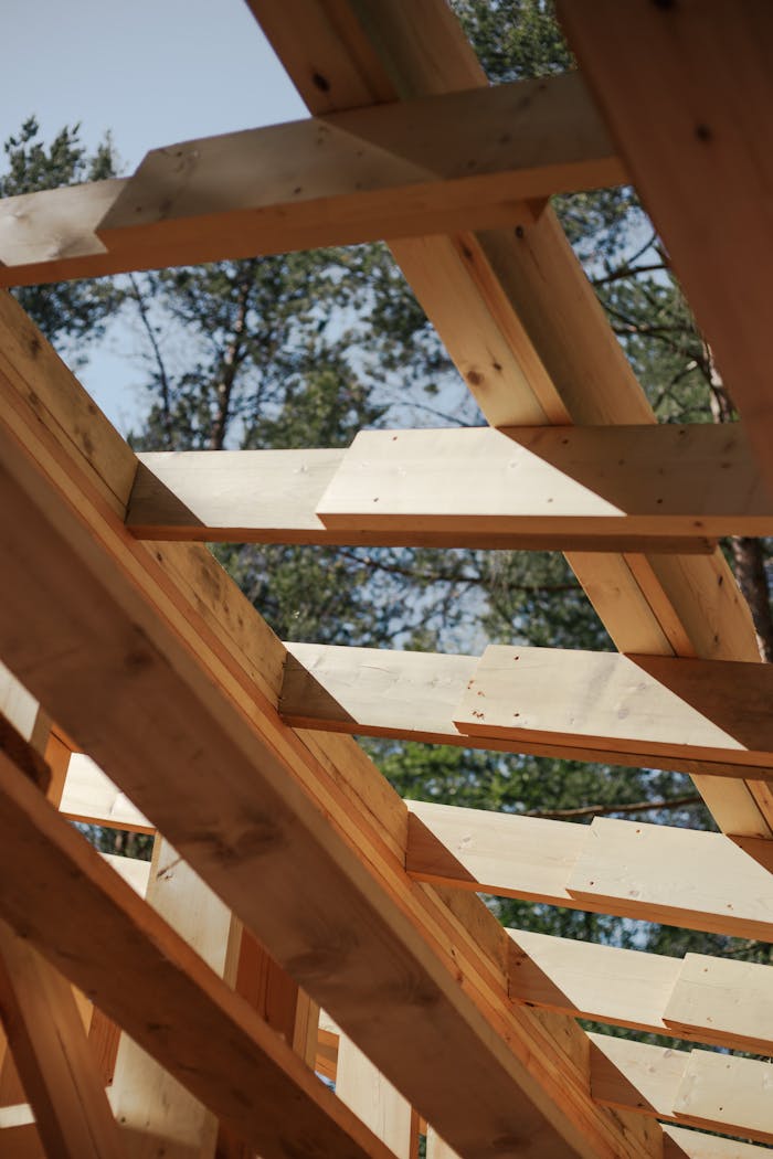 contact-img Close-up view of wooden beams forming a house roof structure against a sky background.